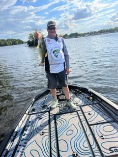 Angler on bass boat holding a fish on a sunny lake, promoting NJ freshwater fishing charters and tours.